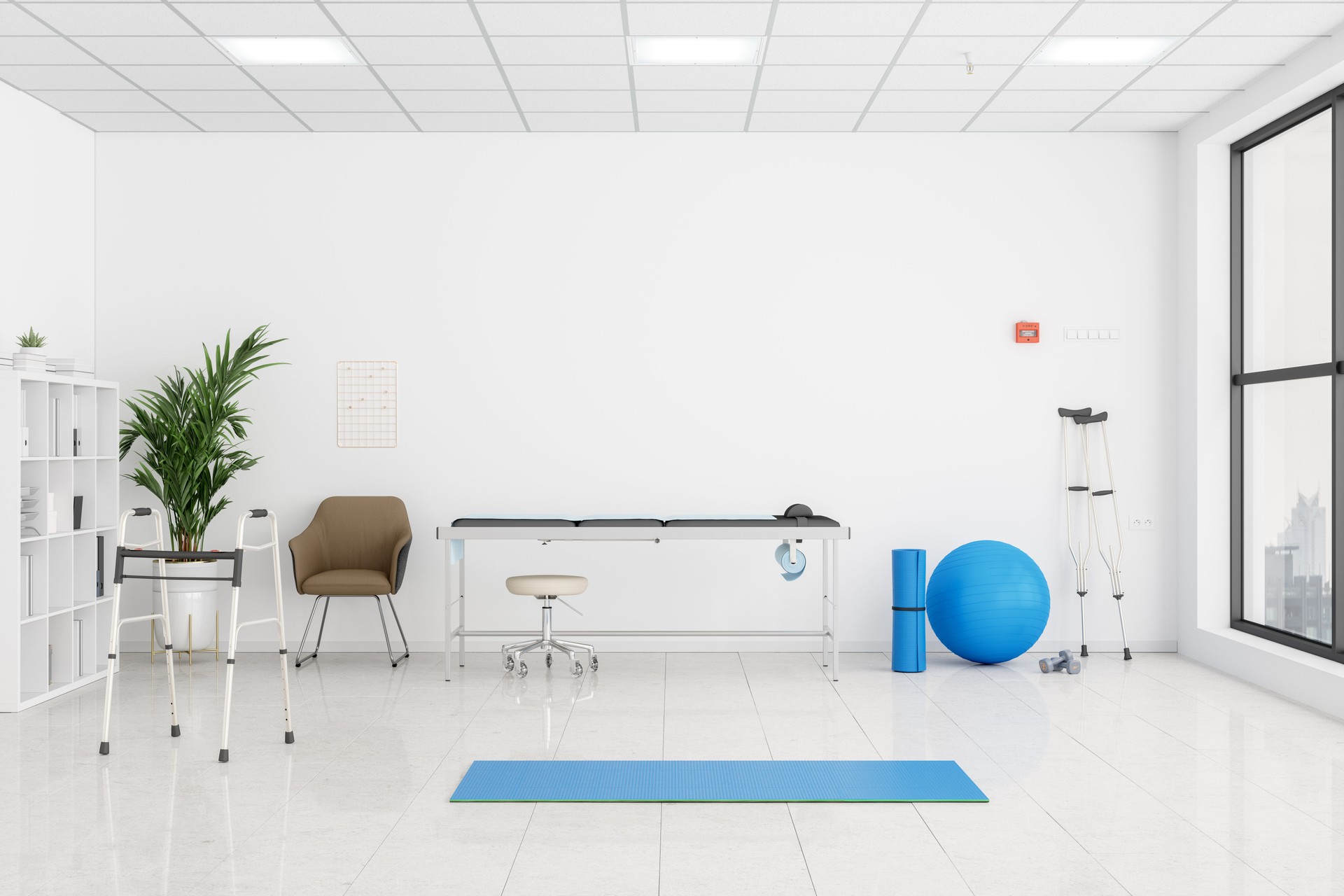 Interior Of A Physical Therapy Room With Examination table, Mobility Walker, Crutch, Blue Colored Fitness Ball And Exercise Mat.